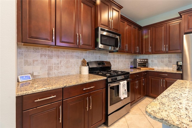 kitchen with stainless steel appliances, light tile patterned flooring, backsplash, and light stone counters