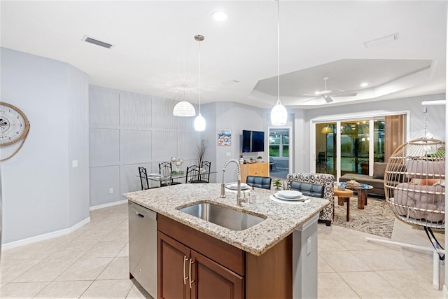 kitchen with sink, a raised ceiling, stainless steel dishwasher, hanging light fixtures, and a center island with sink