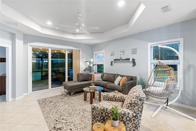 tiled living room with a raised ceiling and ceiling fan