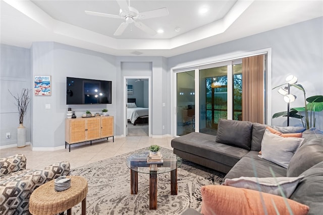 tiled living room with ceiling fan and a tray ceiling