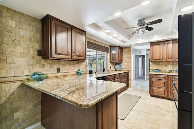 kitchen with light stone counters, kitchen peninsula, sink, and a tray ceiling