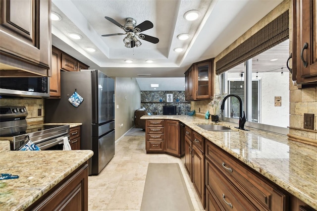 kitchen with appliances with stainless steel finishes, backsplash, light stone counters, a raised ceiling, and sink