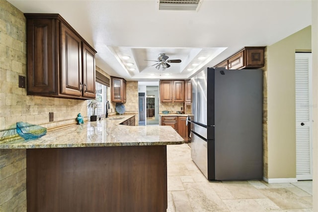 kitchen with kitchen peninsula, stainless steel fridge, backsplash, a raised ceiling, and sink