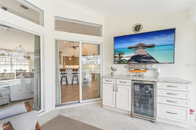 bar featuring light carpet, light stone counters, a wealth of natural light, white cabinets, and wine cooler