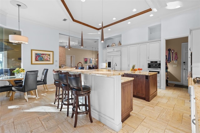 kitchen with a center island with sink, decorative light fixtures, paneled fridge, light stone countertops, and white cabinets