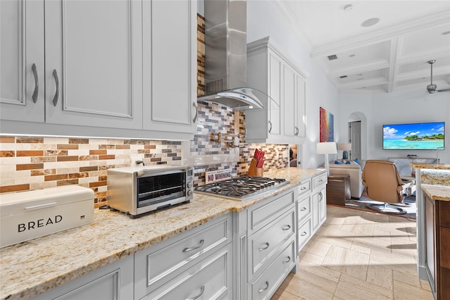 kitchen with stainless steel gas cooktop, light stone countertops, wall chimney exhaust hood, white cabinets, and decorative backsplash