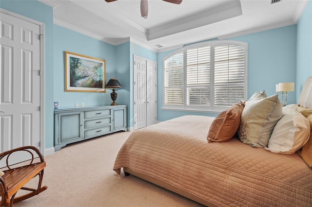 bedroom with a closet, ornamental molding, carpet flooring, a tray ceiling, and ceiling fan