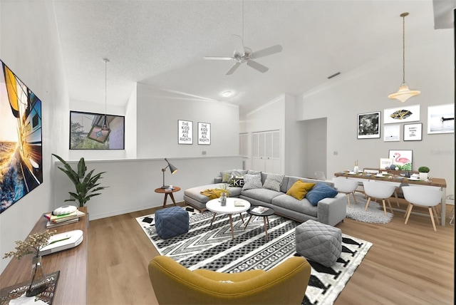 living room with ceiling fan, high vaulted ceiling, hardwood / wood-style floors, and a textured ceiling