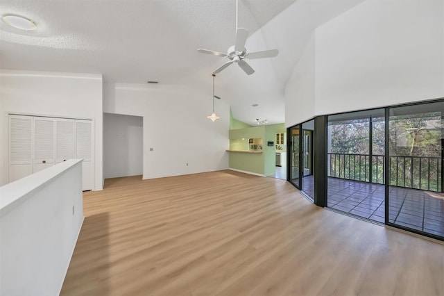 unfurnished living room with a textured ceiling, high vaulted ceiling, ceiling fan, and light wood-type flooring