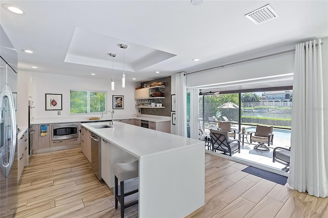 kitchen with built in appliances, a raised ceiling, light wood-type flooring, and hanging light fixtures