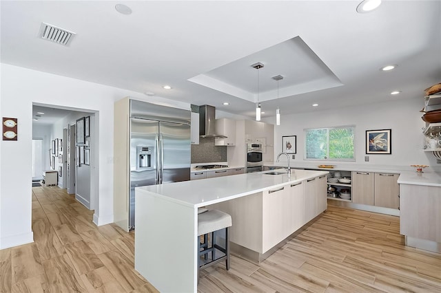 kitchen with wall chimney exhaust hood, decorative light fixtures, light wood-type flooring, and stainless steel appliances