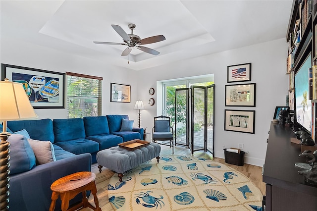 living room featuring hardwood / wood-style flooring, ceiling fan, and a raised ceiling