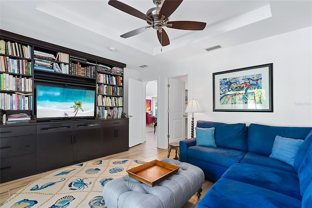 living room featuring light hardwood / wood-style floors, a raised ceiling, and ceiling fan