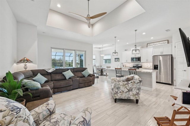 living room featuring light hardwood / wood-style floors, ceiling fan, a tray ceiling, and sink