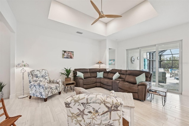 living room featuring a raised ceiling, light hardwood / wood-style flooring, and ceiling fan