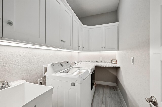 laundry area featuring cabinets, light wood-type flooring, washing machine and dryer, and sink