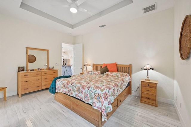 bedroom with a tray ceiling, ceiling fan, and light hardwood / wood-style flooring