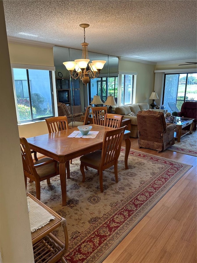 dining area with a textured ceiling, hardwood / wood-style flooring, a wealth of natural light, and a notable chandelier