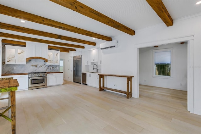 kitchen with an AC wall unit, premium appliances, decorative backsplash, white cabinets, and light hardwood / wood-style flooring