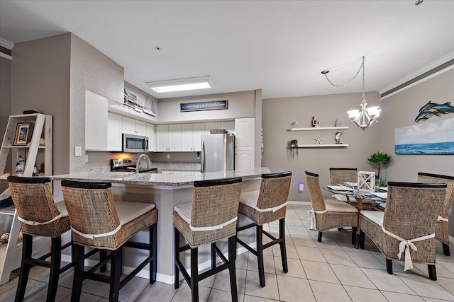 kitchen featuring stainless steel appliances, white cabinetry, a kitchen bar, an inviting chandelier, and kitchen peninsula