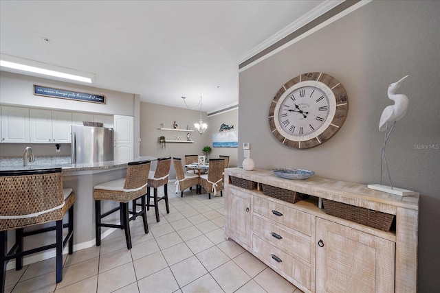 kitchen featuring a breakfast bar, ornamental molding, an inviting chandelier, stainless steel fridge, and pendant lighting