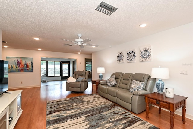 living room with hardwood / wood-style flooring, ceiling fan, and a textured ceiling