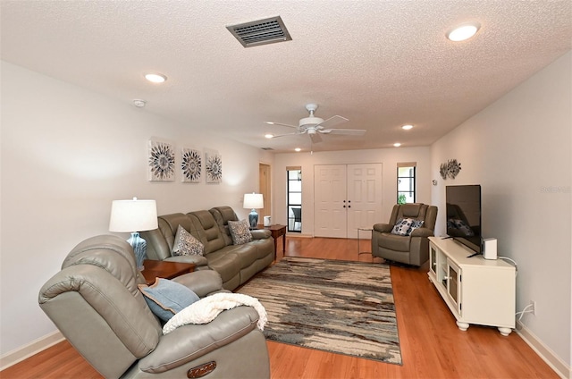 living room with a textured ceiling, light hardwood / wood-style flooring, and ceiling fan