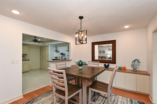 dining space with light hardwood / wood-style floors, ceiling fan with notable chandelier, and a textured ceiling