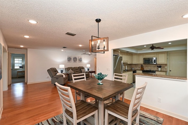 dining area featuring light wood-type flooring, ceiling fan with notable chandelier, and a textured ceiling