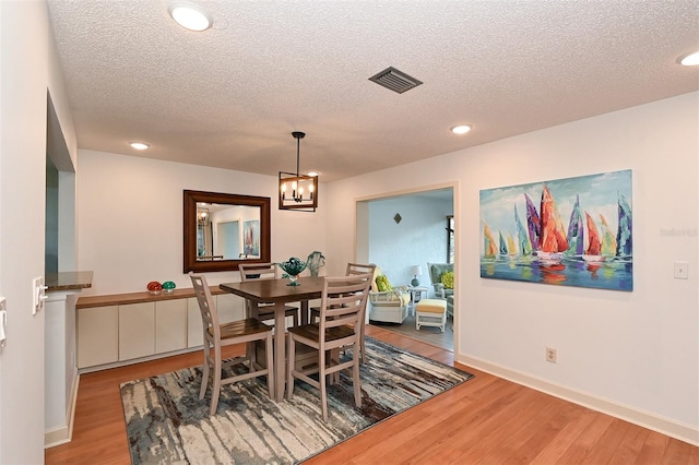 dining area featuring light hardwood / wood-style floors, a textured ceiling, and an inviting chandelier