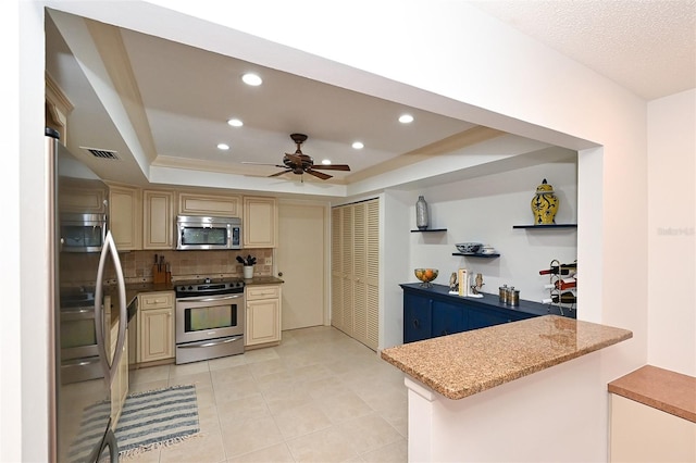 kitchen featuring light stone countertops, a raised ceiling, backsplash, and appliances with stainless steel finishes