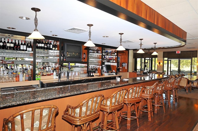 bar with dark stone counters, pendant lighting, and dark wood-type flooring