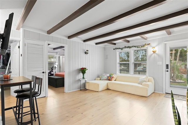 living room with wood walls, beamed ceiling, and light hardwood / wood-style flooring