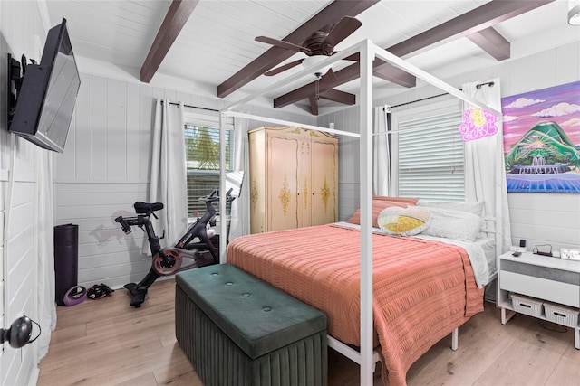 bedroom with wood walls, beamed ceiling, ceiling fan, and light hardwood / wood-style flooring