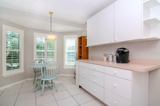 kitchen with a wealth of natural light, white cabinetry, light tile patterned floors, and decorative light fixtures