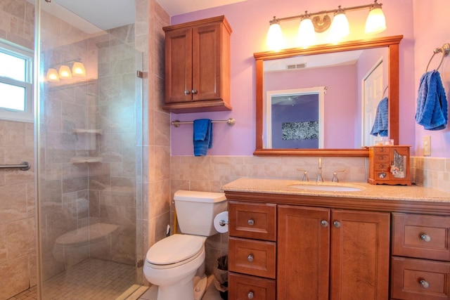 bathroom with toilet, vanity, tile walls, and a tile shower