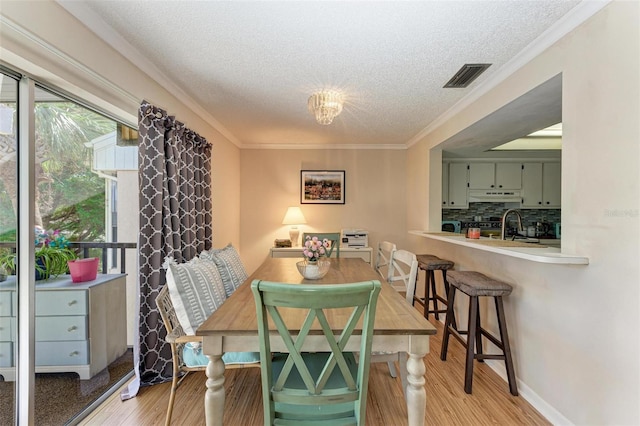 dining area featuring sink, light hardwood / wood-style floors, crown molding, and a textured ceiling