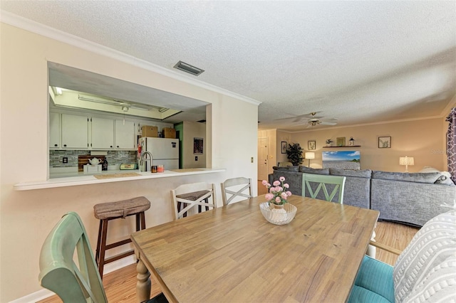 dining space with a textured ceiling, ceiling fan, light wood-type flooring, and crown molding