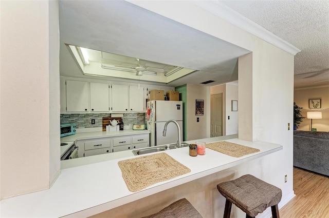 kitchen with kitchen peninsula, white appliances, a tray ceiling, sink, and light hardwood / wood-style flooring