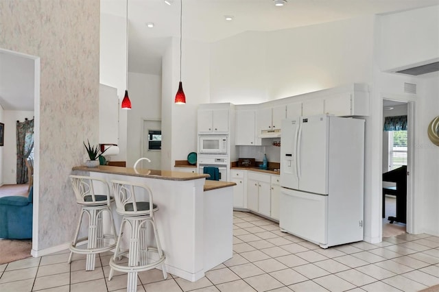 kitchen with kitchen peninsula, white appliances, decorative light fixtures, white cabinetry, and a breakfast bar area