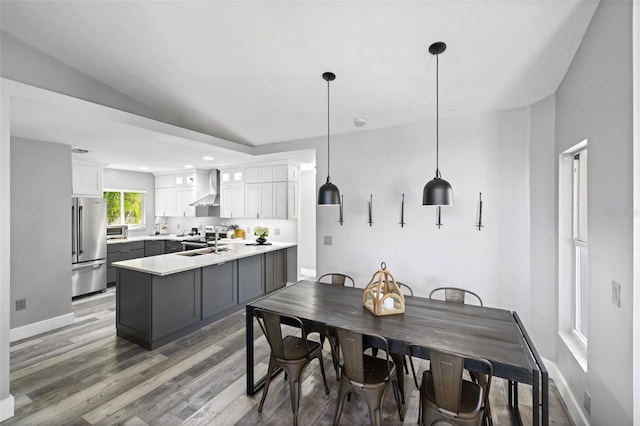 kitchen with lofted ceiling, white cabinets, wall chimney range hood, hanging light fixtures, and appliances with stainless steel finishes