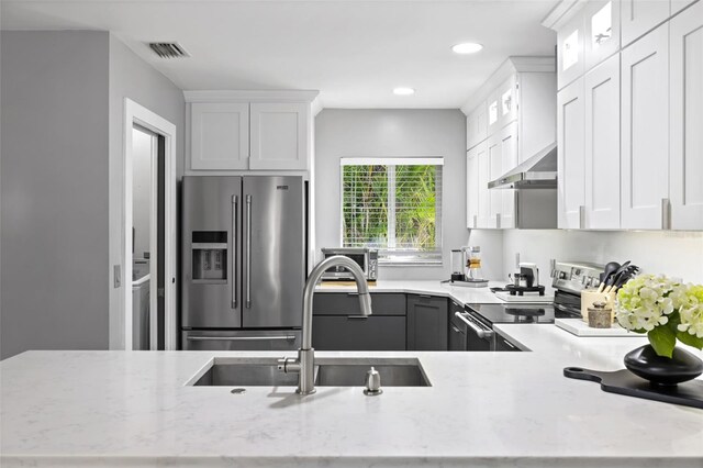 kitchen with white cabinetry, sink, wall chimney exhaust hood, stainless steel appliances, and light stone counters