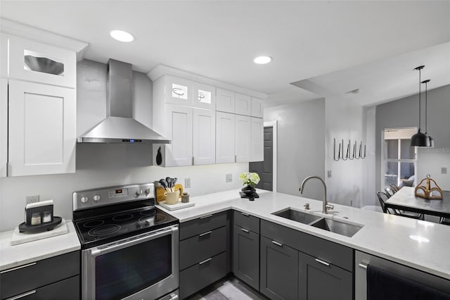 kitchen with appliances with stainless steel finishes, sink, wall chimney range hood, white cabinets, and hanging light fixtures