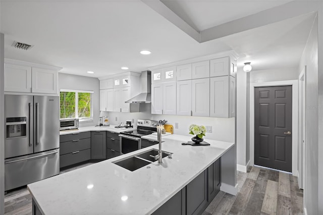 kitchen with white cabinets, hardwood / wood-style flooring, wall chimney exhaust hood, and appliances with stainless steel finishes