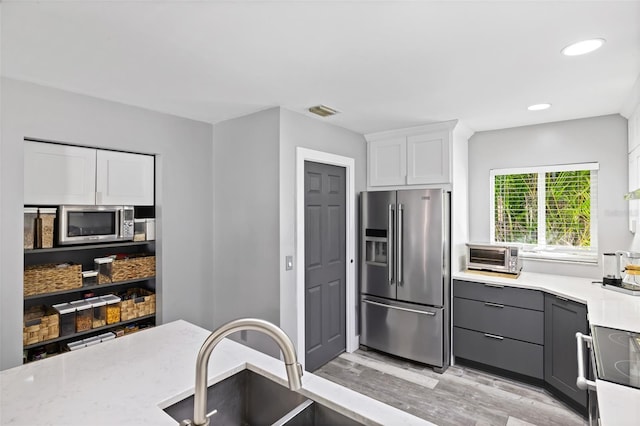 kitchen with light stone counters, light hardwood / wood-style floors, gray cabinets, white cabinets, and appliances with stainless steel finishes