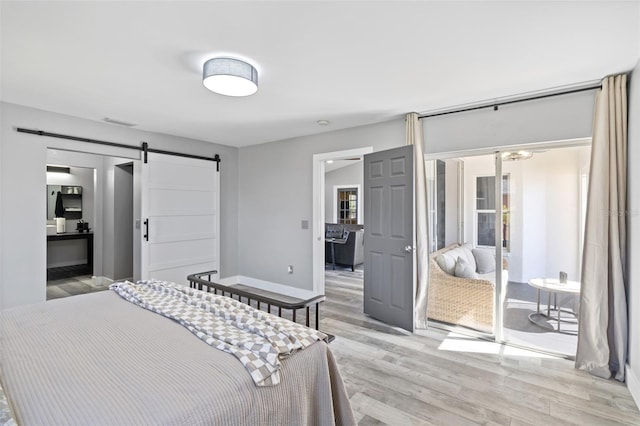 bedroom with a barn door, light hardwood / wood-style flooring, and multiple windows