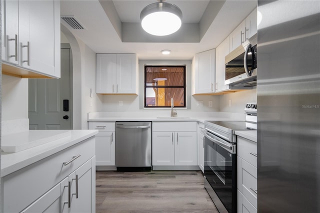 kitchen with white cabinets, light wood-type flooring, stainless steel appliances, and sink