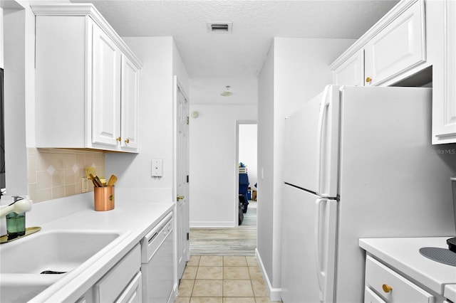 kitchen with backsplash, white appliances, a textured ceiling, light tile patterned floors, and white cabinetry