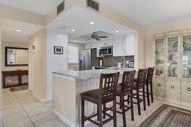 kitchen featuring kitchen peninsula, a kitchen breakfast bar, light stone counters, stainless steel appliances, and white cabinets