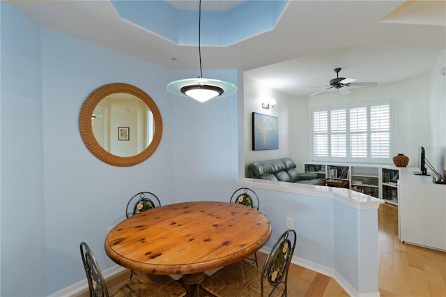 dining space with a tray ceiling, ceiling fan, and light hardwood / wood-style flooring